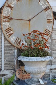 an old rusty clock sitting on top of a white planter filled with orange flowers