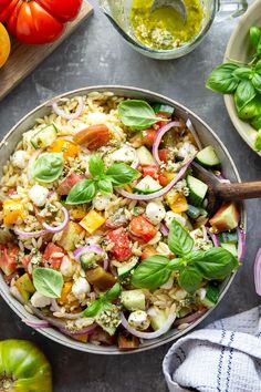 a bowl filled with pasta salad next to tomatoes, onions and other vegetables on a table