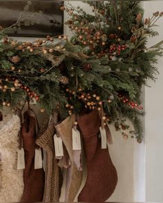 stockings hanging from the wall with christmas decorations on them and pine cones, berries, and other greenery