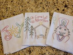 three embroidered napkins with the words, oh come let us adore him