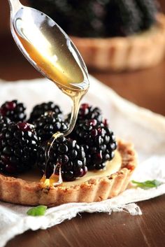 a person pouring syrup onto a tart topped with blackberries