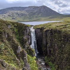 a waterfall in the middle of a mountain range with water running down it's side