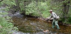 a man standing in the middle of a river holding a fishing rod and looking down at it