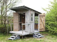 an outhouse in the middle of a field with steps leading up to it and trees around