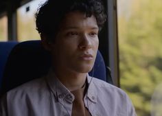 a young man sitting on a bus wearing headphones and looking off into the distance