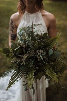 a woman in a white dress holding a bouquet of flowers and greenery on her wedding day