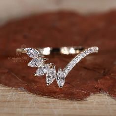 a close up view of a diamond ring with leaves on it's side, sitting on a piece of wood