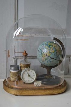 an old globe under a glass dome on a wooden stand with other items underneath it