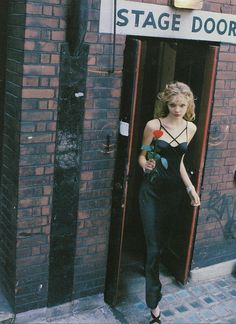 a woman standing in front of a brick building with a sign that says stage door