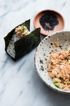 a white bowl filled with food next to two small plates on a table top and one has sushi in it