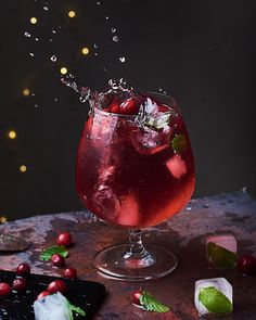 a red drink with ice and cherries splashing into the glass on a table