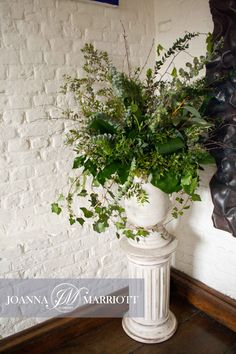 a white vase filled with lots of greenery sitting on top of a wooden table