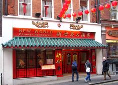 two people walking past a chinese restaurant on the side of a street with red lanterns hanging above it