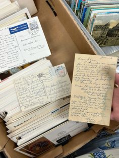 an open box filled with lots of papers and envelopes next to a person's hand