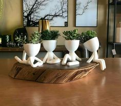 three white ceramic planters sitting on top of a wooden table in front of paintings