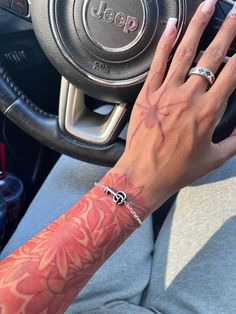 a woman's hand on the steering wheel of a car, with tattoos on her arm