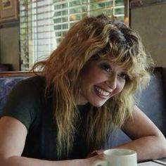 a woman sitting at a table with a coffee cup in front of her and smiling