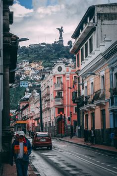 a man walking down a street next to tall buildings with a statue in the background