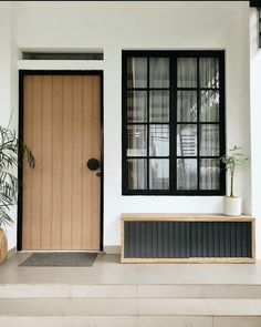 a white house with black trim and wooden doors, planters on the front steps