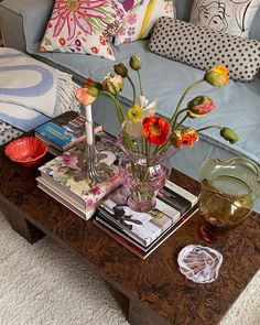 a coffee table with flowers and books on it in front of a blue couch covered in pillows