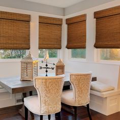 two chairs sitting at a table in front of windows with roman shades on the windowsill