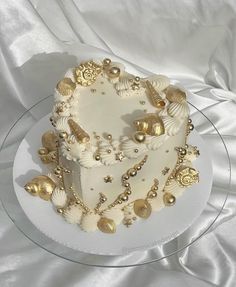 a heart shaped cake decorated with seashells and gold decorations on a clear plate