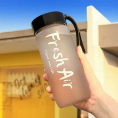 a person holding a water bottle with the words fresh air written on it in front of a building