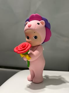 a pink bear holding a red rose on top of a white table next to a gray wall