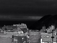 black and white photograph of rooftops with dark clouds in the sky behind them,