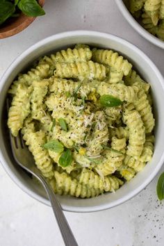 two white bowls filled with pasta and pesto on top of a marble countertop