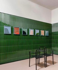 two black chairs sitting next to each other in front of a green wall with pictures on it