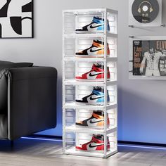 a stacking rack with several pairs of shoes in front of a black couch and blue wall