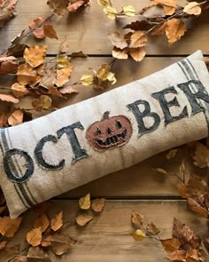 an embroidered pillow that says october with a pumpkin on it and leaves scattered around it