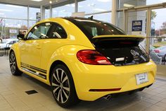 the back end of a yellow volkswagen beetle parked in a showroom with its trunk open