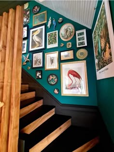 the stairs are covered with pictures and framed art on green walls, along with wooden handrails