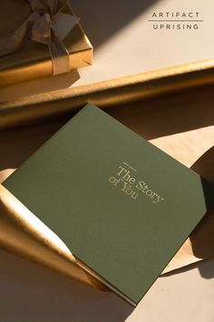 a green book sitting on top of a table next to a gold tray with a bow