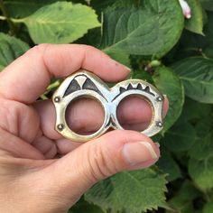 a person holding a small metal ring in their hand with leaves around it and bushes behind them