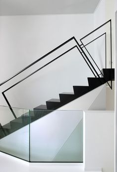 a staircase with glass railing and handrails in a white walled room next to a window