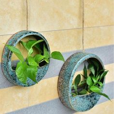 two round metal planters with green plants in them on the side of a wall