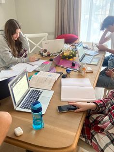 three people sitting at a table with laptops and notebooks on top of it