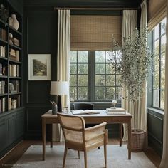 a home office with dark green walls and white carpeted flooring, along with a large window covered in sheer drapes