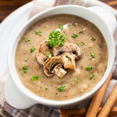 a white bowl filled with mushroom soup next to some cinnamon sticks and green garnish