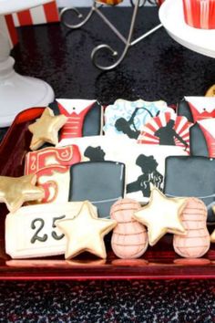 decorated cookies are displayed on a tray in front of a plate with cupcakes