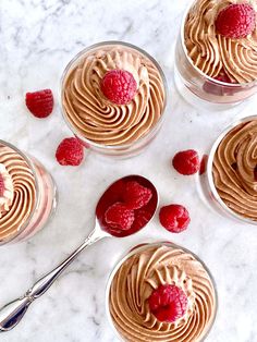 four small desserts with raspberries and whipped cream in them on a marble surface