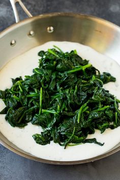 spinach is being cooked in a pan on the stove top with white sauce over it