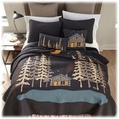 a bed covered in a black comforter with trees on it and a cabin at night