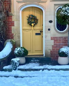 a yellow front door with two planters and a wreath on it