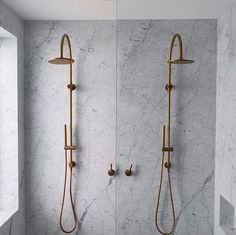 two gold shower faucets in a bathroom with white marble walls and flooring