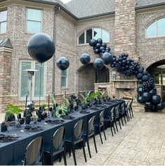 a long table is set up outside with black balloons and greenery on the tables