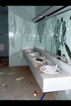 a bathroom with broken glass on the wall and two sinks in the foreground, surrounded by debris